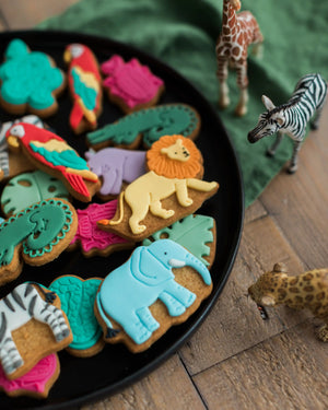 Honeywell Bakes Personalised Jar of Safari Biscuits - Decorative cookies shaped like animals on a black plate with toy animal figures around.