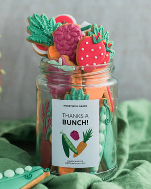 Honeywell Bakes Personalised Gardeners Fruit and Vegetable Biscuit Jar - Jar of colourful cookie cutters with a 'Thanks a Bunch!' label on a green fabric background