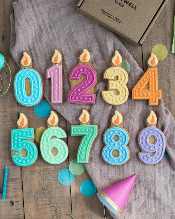 Honeywell Bakes Pick Your Own Milestone Birthday Biscuits - Colourful number cookies with candle decorations on a wooden surface.