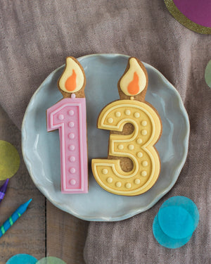 Honeywell Bakes Pick Your Own Milestone Birthday Biscuits - Number 13 cookies with candles on a plate, surrounded by colourful confetti on a wooden surface.