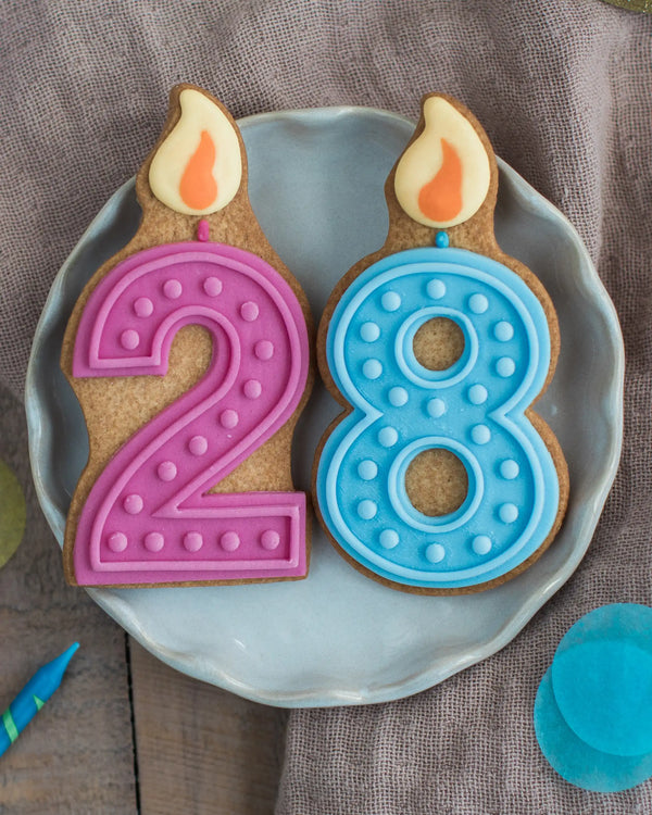 Honeywell Bakes Pick Your Own Milestone Birthday Biscuits - Two cookie candles shaped like the number 28 on a plate with a brown fabric background.