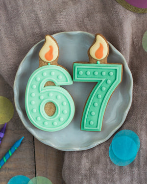 Honeywell Bakes Pick Your Own Milestone Birthday Biscuits - Number 67 cookies with candles on a plate against a brown background