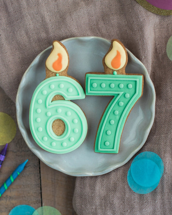 Honeywell Bakes Pick Your Own Milestone Birthday Biscuits - Number 67 cookies with candles on a plate against a brown background