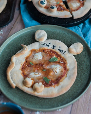 Honeywell Bakes Pizza Pet Baking Kit - Small pizza shaped like a mouse on a green plate with a blue napkin in the background.
