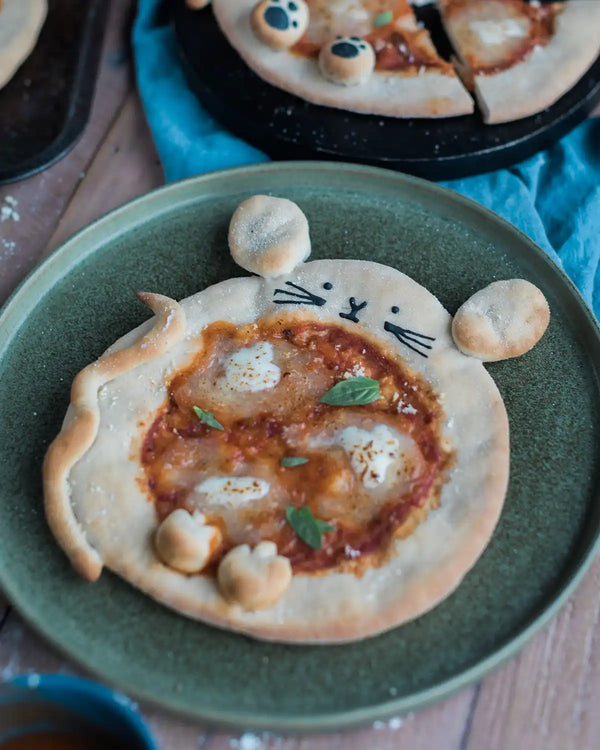 Honeywell Bakes Pizza Pet Baking Kit - Small pizza shaped like a mouse on a green plate with a blue napkin in the background.