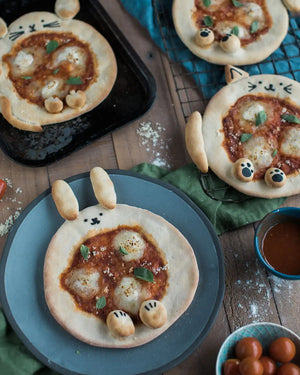 Honeywell Bakes Pizza Pet Baking Kit - Pizzas shaped like animals on a wooden table with ingredients and tools.