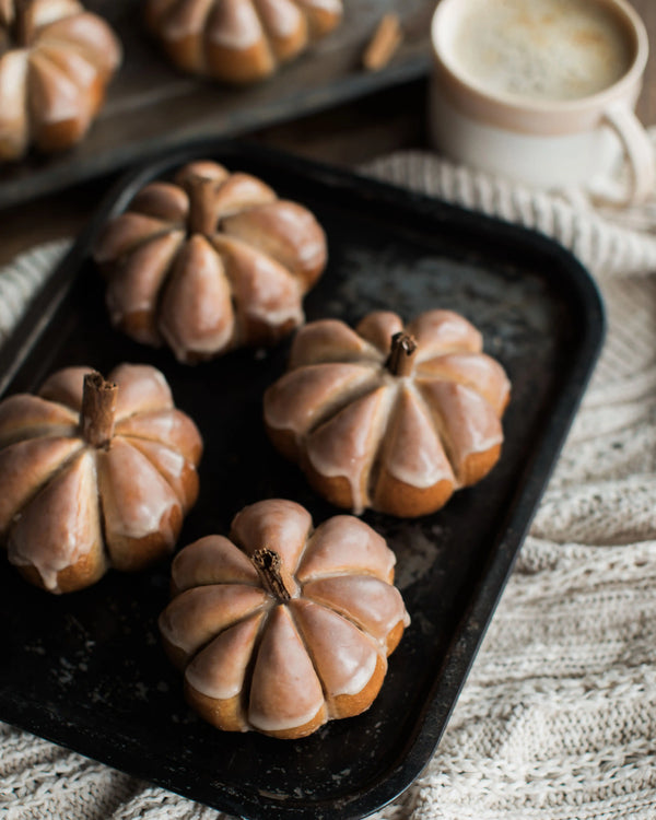 Honeywell Bakes Pumpkin Spiced Iced Bun Baking Kit - Decorative pumpkins on a dark tray with a cup of coffee in the background