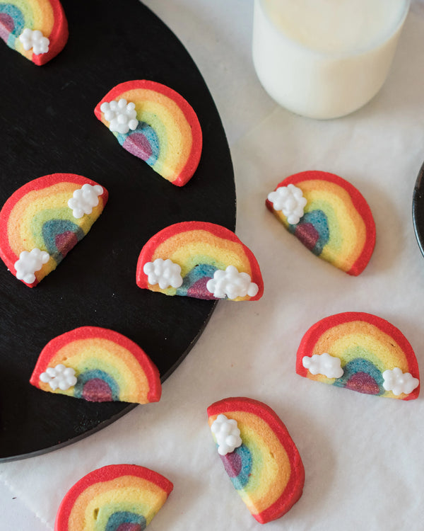 Honeywell Bakes Rainbow Biscuit Baking Kit - Rainbow-shaped cookies with white frosting clouds on a black plate and white surface.