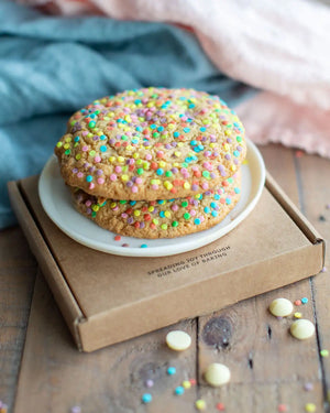 Honeywell Bakes Rainbow Sprinkle Cookie Kit - Two cookies with colourful sprinkles on a white plate on top of a brown box on a wooden surface.