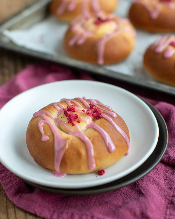 Honeywell Bakes Bakers Club Subscription, A golden-brown baked pastry with pink icing drizzle and raspberry topping