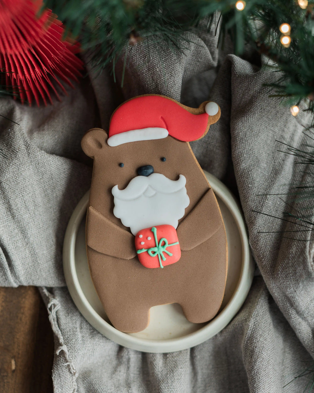 Honeywell Bakes Santa Paws Biscuit Bear - Hand holding a bear-shaped cookie with Santa hat and gift, Christmas decorations in the background