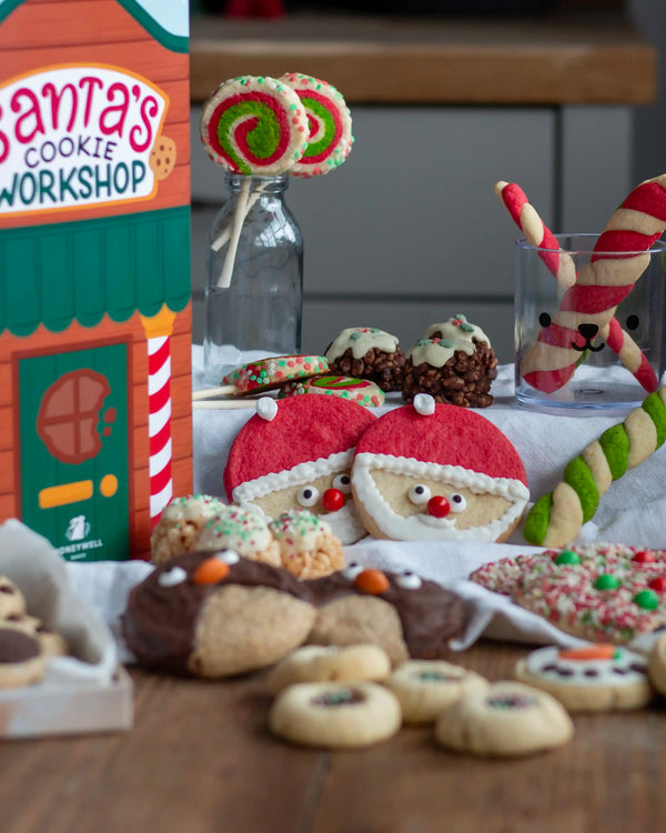 Honeywell Bakes Santa’s Cookie Workshop - 12 Days Christmas Baking Advent - A styled holiday cookie display with assorted decorated cookies, candy canes, lollipops, and a Santa's Cookie Workshop sign on a wooden table.