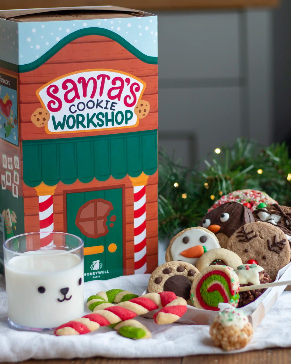 Honeywell Bakes Santa’s Cookie Workshop - 12 Days Christmas Baking Advent - Santa's Cookie Workshop gift set featuring a decorated cardboard box, assorted decorated cookies, candy canes, and a glass of milk on a table with holiday greenery in the background.