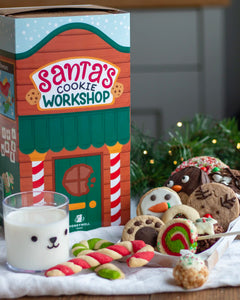 Honeywell Bakes Santa’s Cookie Workshop - 12 Days Christmas Baking Advent - Santa's Cookie Workshop gift set featuring a decorated cardboard box, assorted decorated cookies, candy canes, and a glass of milk on a table with holiday greenery in the background.