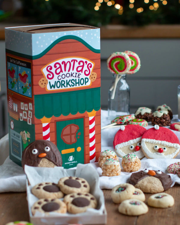 Honeywell Bakes Santa’s Cookie Workshop - 12 Days Christmas Baking Advent - A festive Christmas-themed cookie gift set displayed on a wooden table, featuring a colourful 'Santa's Cookie Workshop' box, assorted decorated cookies, and lollipops in the background.