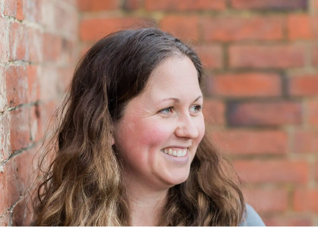 Woman with wavy hair smiling against a brick wall