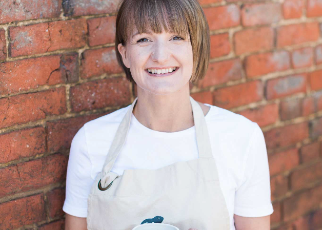 Person wearing a white apron holding a mug against a brick wall