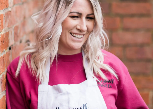 Woman wearing a pink apron and holding a mug against a brick wall
