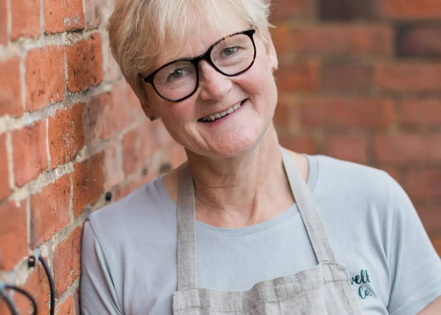 Person wearing a gray apron leaning against a brick wall