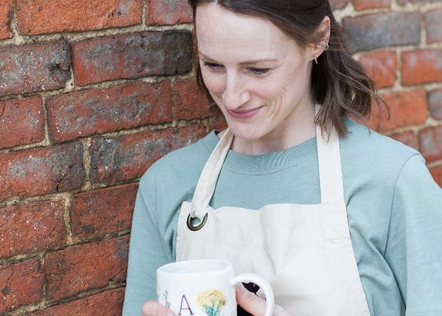 Woman holding a mug with a floral design against a brick wall