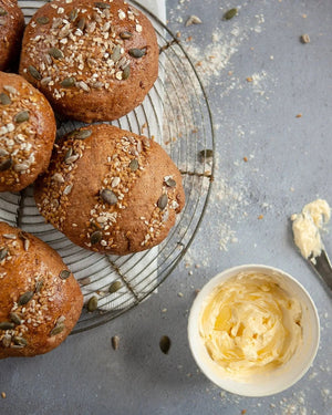 Honeywell Bakes Bread Bakers Subscription, home baked bread rolls with seeds on a cooling rack next to a bowl of butter.