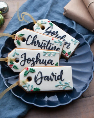 Honeywell Bakes Six Personalised Christmas Tag Biscuits - Decorative cookies shaped like name tags with personalized names on a blue plate.