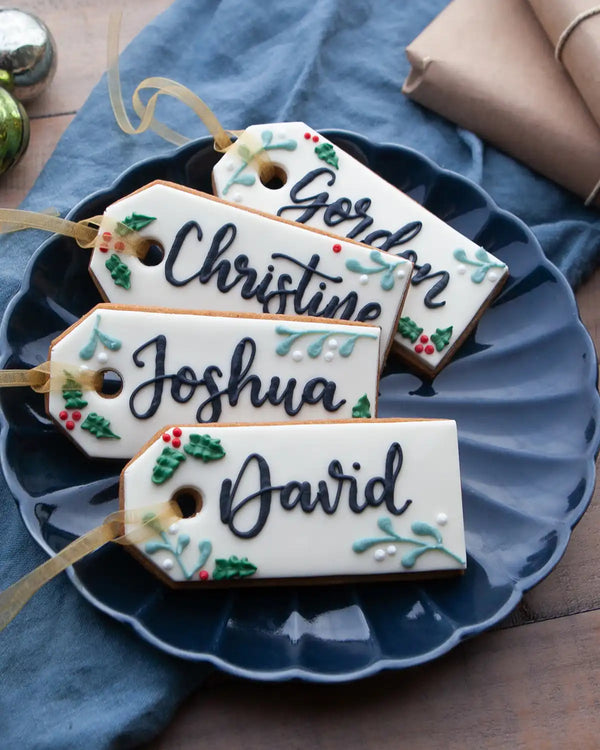 Honeywell Bakes Six Personalised Christmas Tag Biscuits - Decorative cookies shaped like name tags with personalized names on a blue plate.