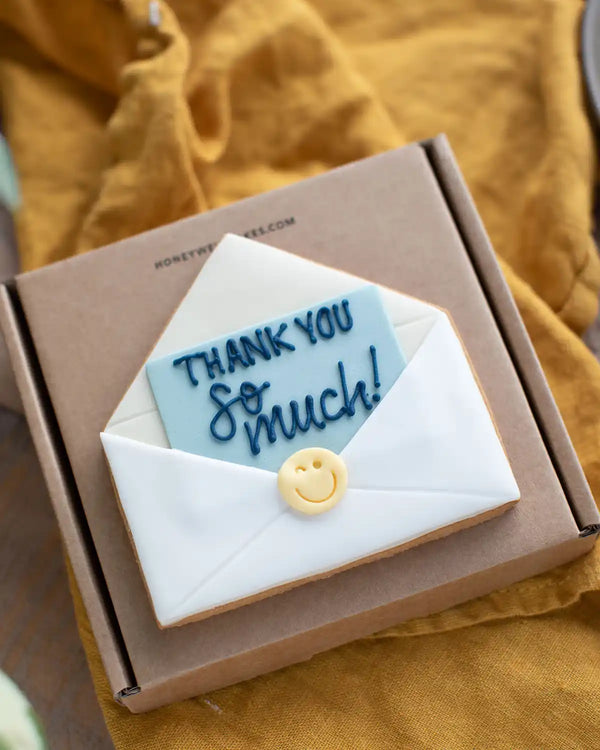 Honeywell Bakes Thank You Biscuit - Cookie shaped like an envelope with 'Thank you so much!' text inside a box on a yellow fabric background.