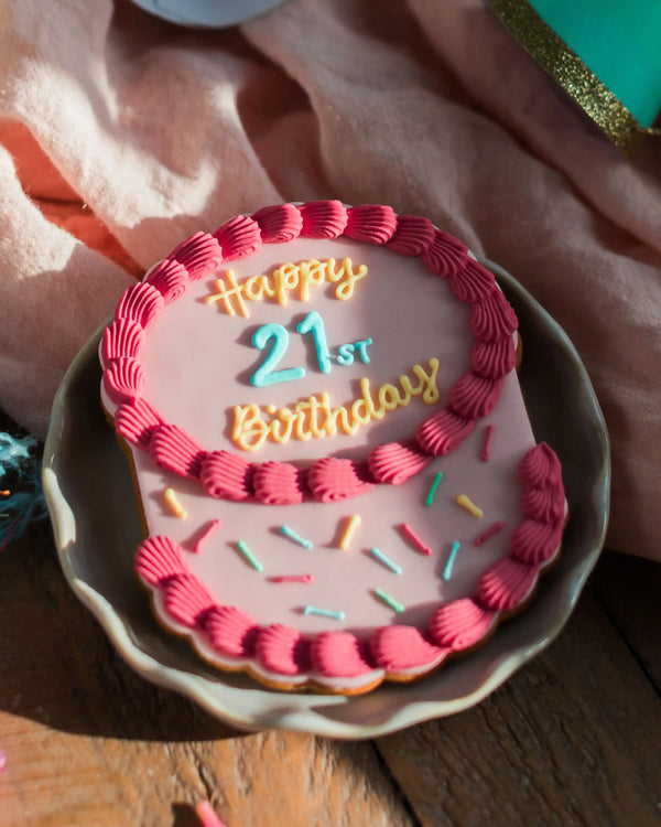 Honeywell Bakes The Big Birthday Biscuit - Pretty In Pink - Small round birthday cake with pink icing and 'Happy 21st Birthday' text on a wooden surface.