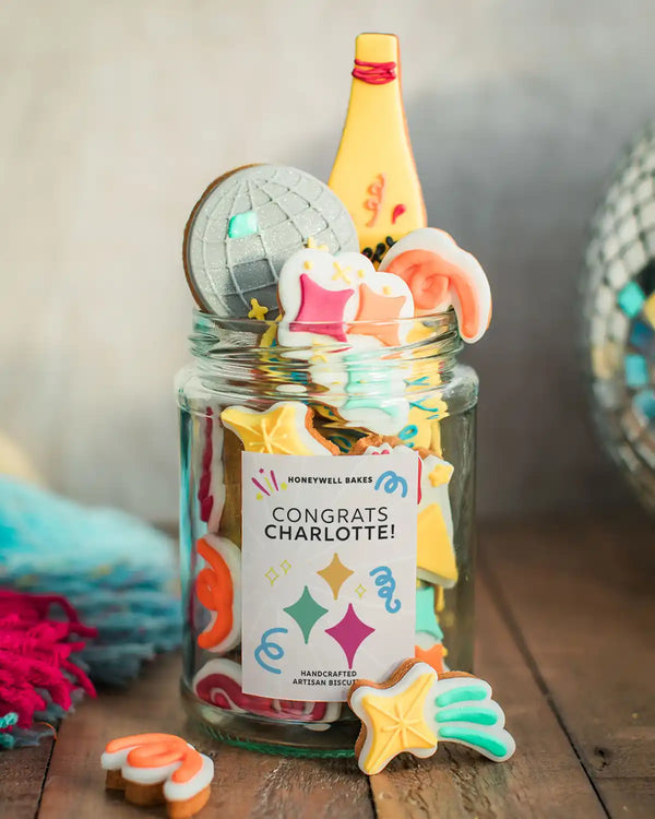 Honeywell Bakes The Celebration Jar - Jar of colourful cookie-shaped candles with a personalised label on a wooden surface.