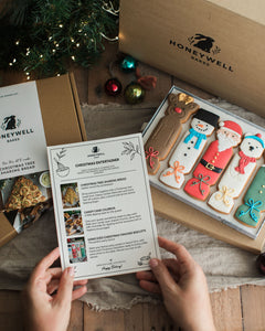 The Christmas Entertainer Bundle by Honeywell Bakes, featuring hand-iced Christmas cracker biscuits, a Christmas tree sharing bread baking kit and chocolate-dipped candy cane churros, presented in festive gift packaging.