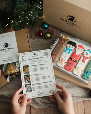 The Christmas Entertainer Bundle by Honeywell Bakes, featuring hand-iced Christmas cracker biscuits, a Christmas tree sharing bread baking kit and chocolate-dipped candy cane churros, presented in festive gift packaging.