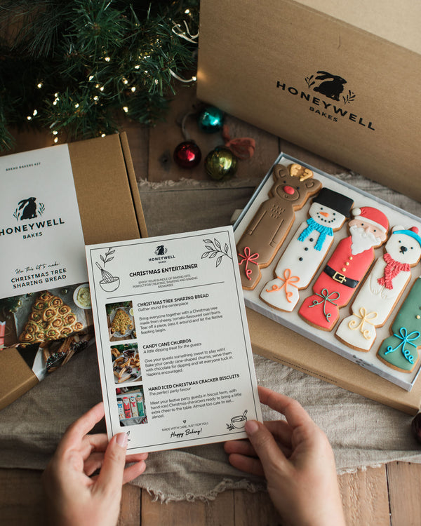 The Christmas Entertainer Bundle by Honeywell Bakes, featuring hand-iced Christmas cracker biscuits, a Christmas tree sharing bread baking kit and chocolate-dipped candy cane churros, presented in festive gift packaging.
