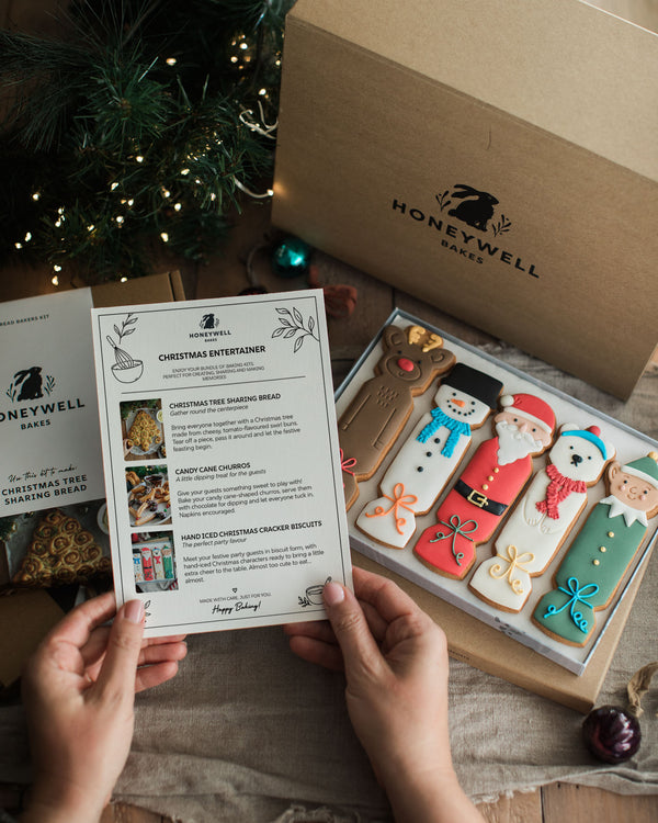 The Christmas Entertainer Bundle by Honeywell Bakes, featuring hand-iced Christmas cracker biscuits, a Christmas tree sharing bread baking kit and chocolate-dipped candy cane churros, presented in festive gift packaging.