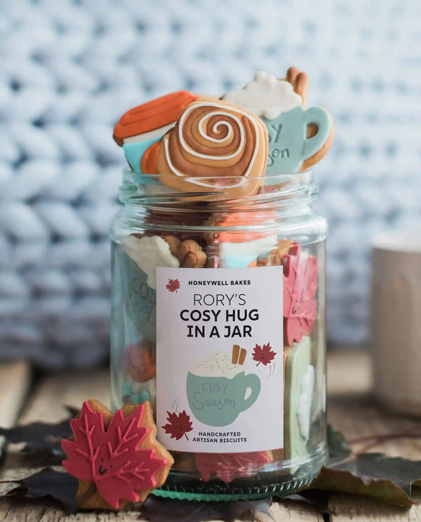 Honeywell Bakes The Cosy Biscuit Jar - A glass mason jar filled with assorted decorated cookies shaped like fall treats, with a white label reading 'Rory's Cosy Hug in a Jar' on a rustic wooden surface.