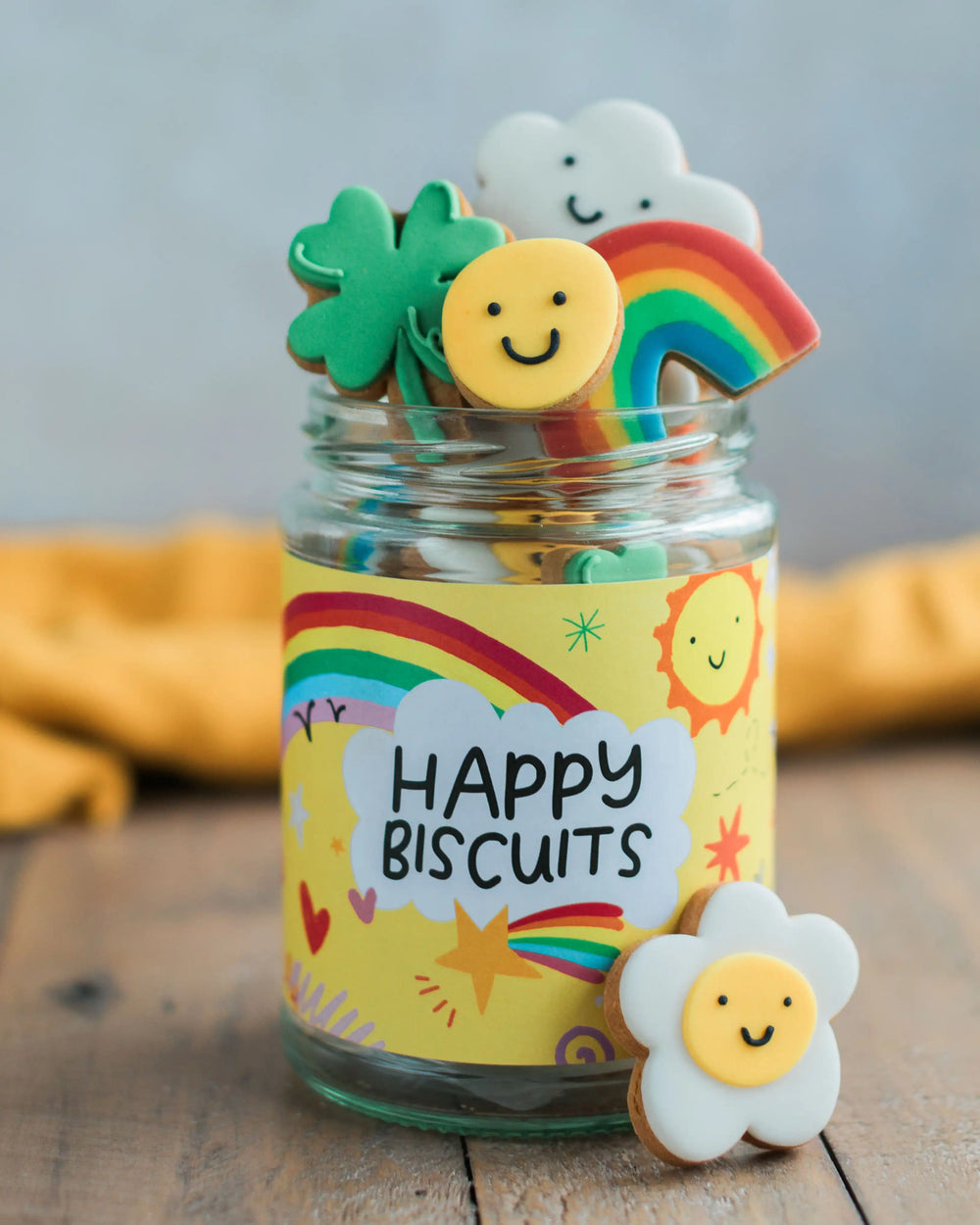 Honeywell Bakes The Happy News Biscuit Jar - Jar of colourful cookies with a 'Happy Biscuits' label on a wooden surface
