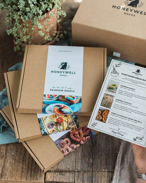 Plant Based Bread Bundle - Honeywell Bakes gift box set on a rustic wooden table, featuring kraft paper boxes, printed recipe cards, and a potted plant in the background.