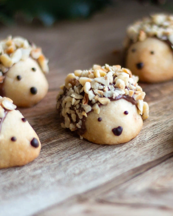 The Woodland Baking Kit Collection - Hedgehog-shaped cookies decorated with chopped nuts on top, chocolate face details, arranged on a rustic wooden surface.
