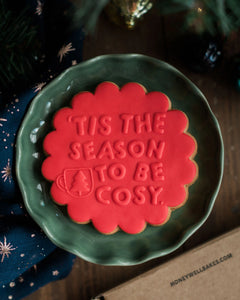 Honeywell Bakes Tis The Season Biscuit - Red cookie with 'Tis the Season to be Cosy' text on a green plate, Christmas tree in background