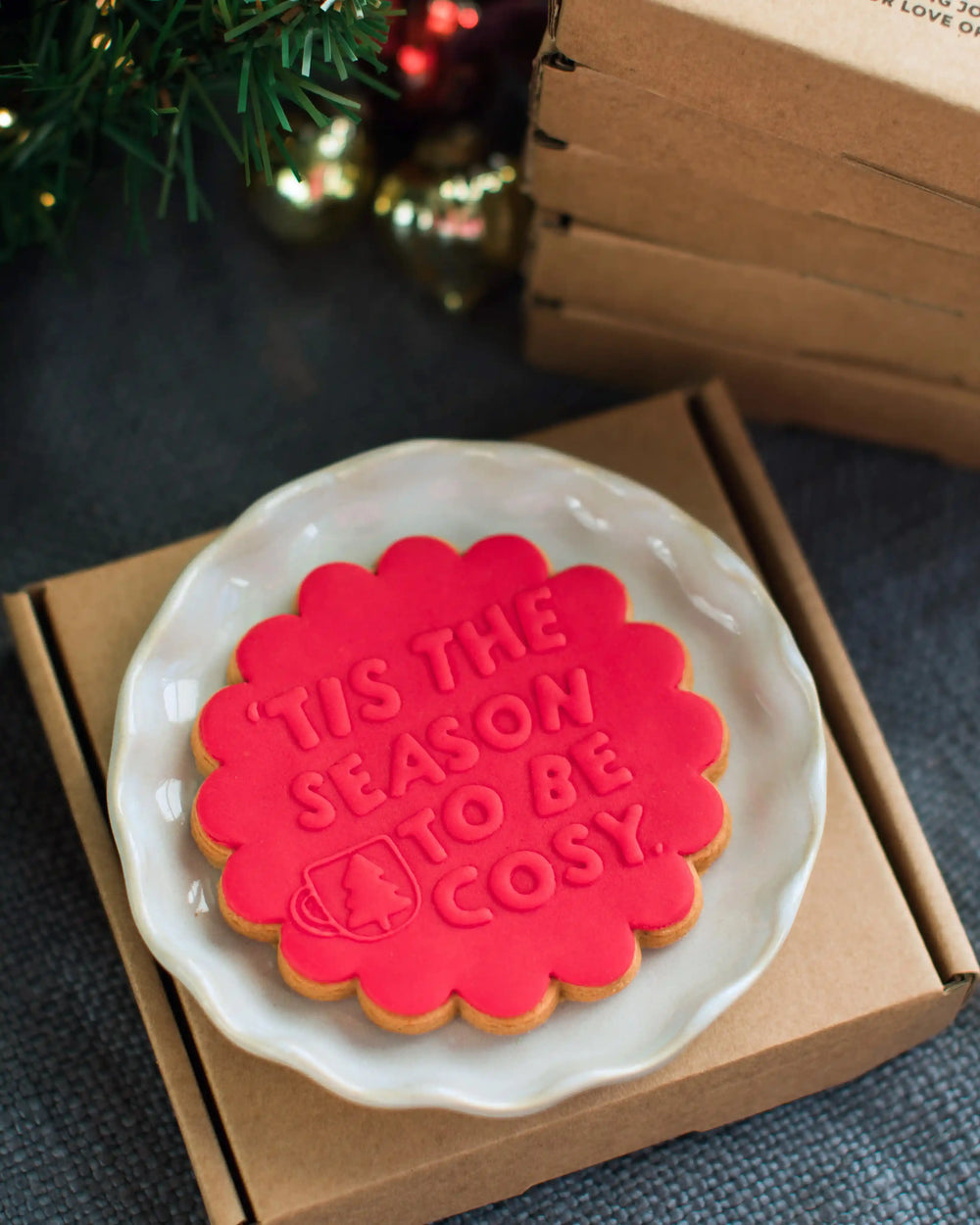 Honeywell Bakes Tis The Season Biscuit x 5 - Red cookie with 'Tis the season to be cozy' text on a white plate, placed inside a cardboard box.