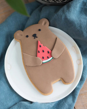 Honeywell Bakes Watermelon Biscuit Bear - Bear-shaped cookie holding a slice of watermelon on a white plate with a blue cloth background