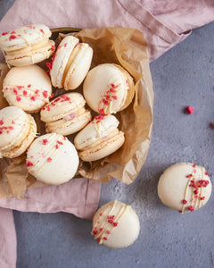 Honeywell Bakes White Chocolate & Raspberry Macaron Kit - White macarons with raspberry pieces and white chocolate drizzle on a grey surface.