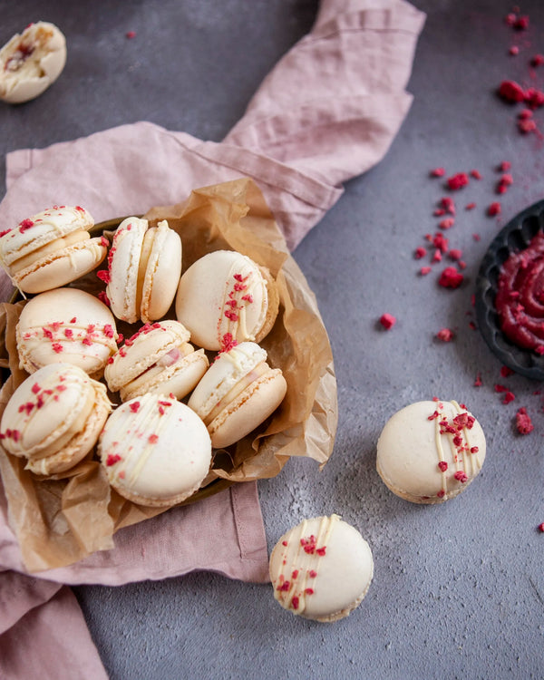 Honeywell Bakes White Chocolate & Raspberry Macaron Kit - White macarons with raspberry pieces and white chocolate drizzle on a grey surface.