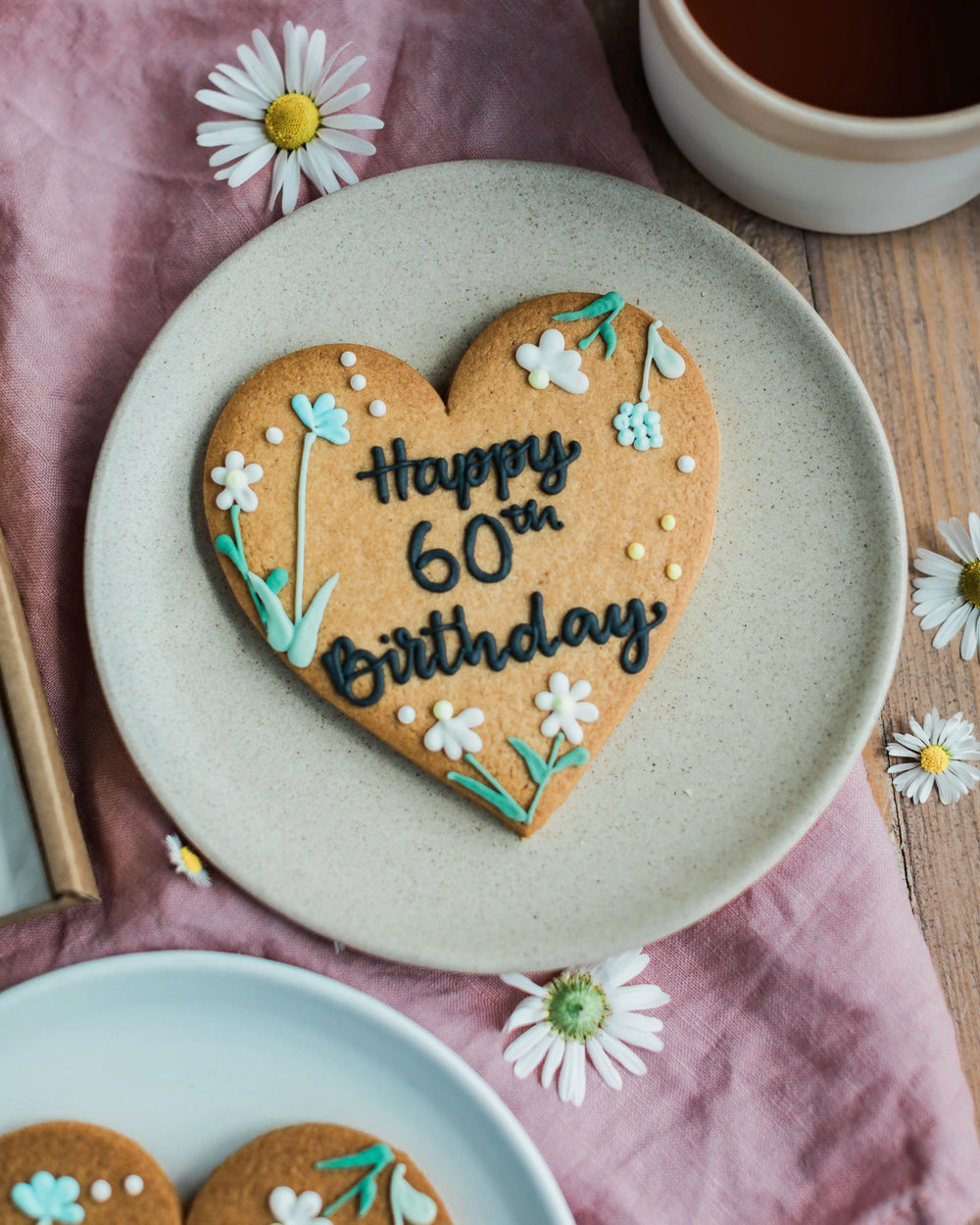 Honeywell Bakes Wildflower Heart – Piped Personalised Biscuit - Heart-shaped cookie with 'You are amazing' text in a box on a pink cloth.