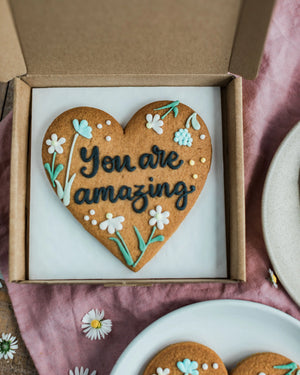 Honeywell Bakes Wildflower Heart – Piped Personalised Biscuit - Heart-shaped cookie with 'You are amazing' text in a box on a pink cloth.