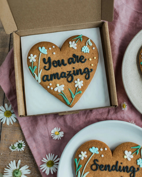 Honeywell Bakes Wildflower Heart – Piped Personalised Biscuit - Heart-shaped cookie with 'You are amazing' text in a box on a pink fabric background.