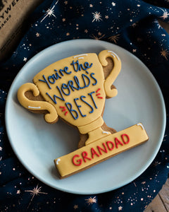 Honeywell Bakes You’re The World's Best - Personalised Trophy Biscuit - Cookie shaped like a trophy with 'You're the world's best grandad' text on a blue plate.