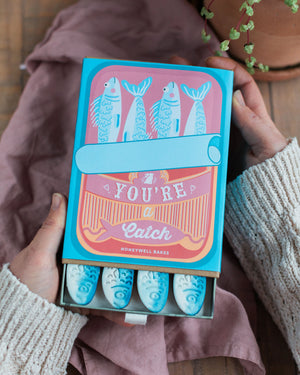 Honeywell Bakes You're a Catch Biscuit Gift Set - Box of 'You're a Catch' hand iced vanilla biscuits held by two hands on a wooden surface.