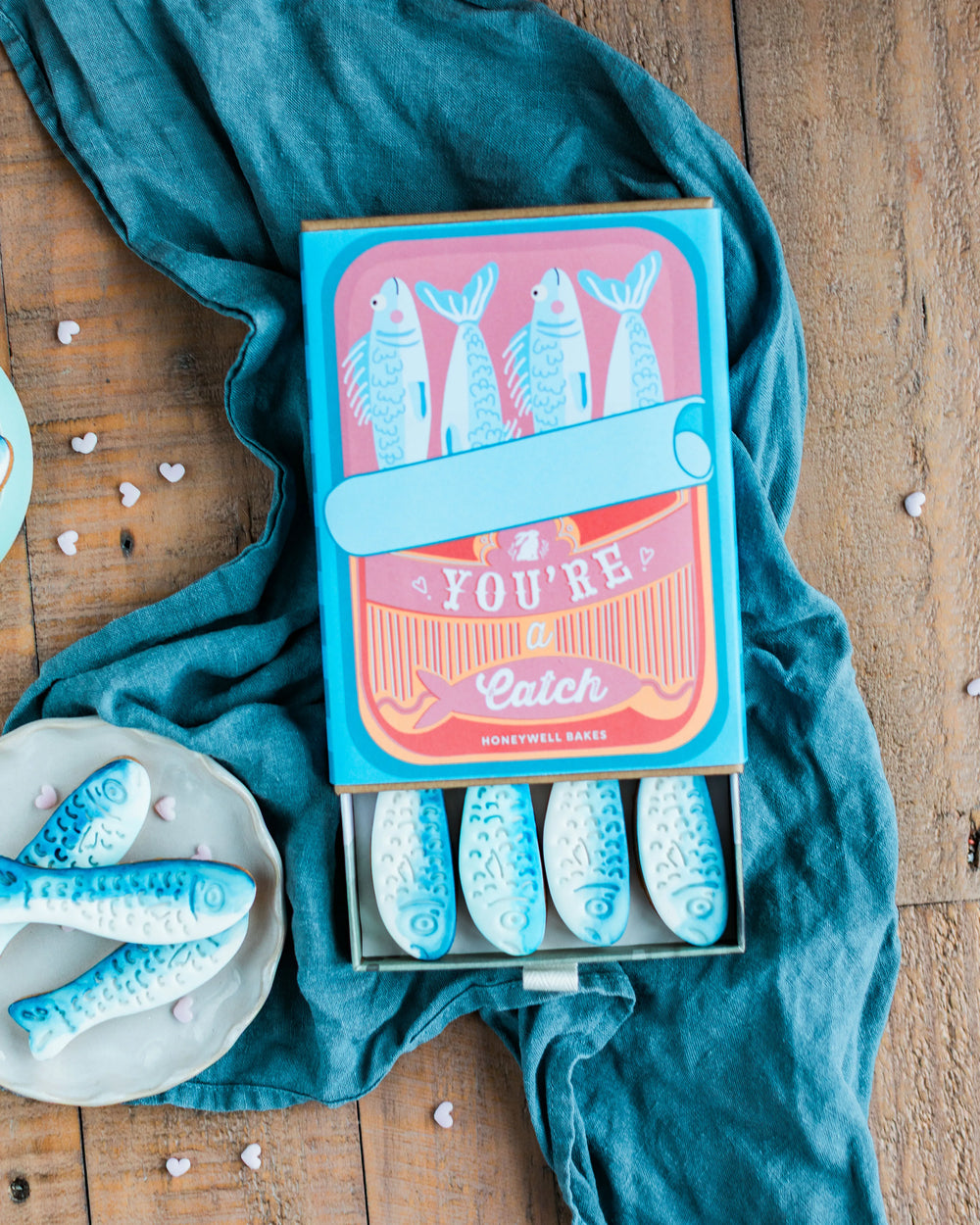 Honeywell Bakes You're a Catch Biscuit Gift Set - packaging with blue sardine fish-shaped hand iced vanilla cookies on a wooden table.