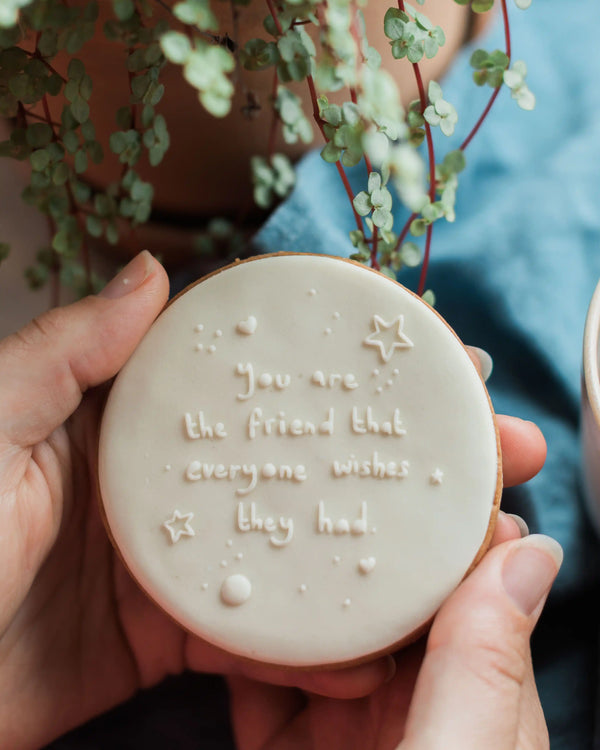 Honeywell Bakes You’re the Best Friend - Person holding a round biscuit with embossed text and star designs, surrounded by greenery.
